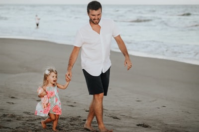 A man holding her daughter take a walk along the coastline
